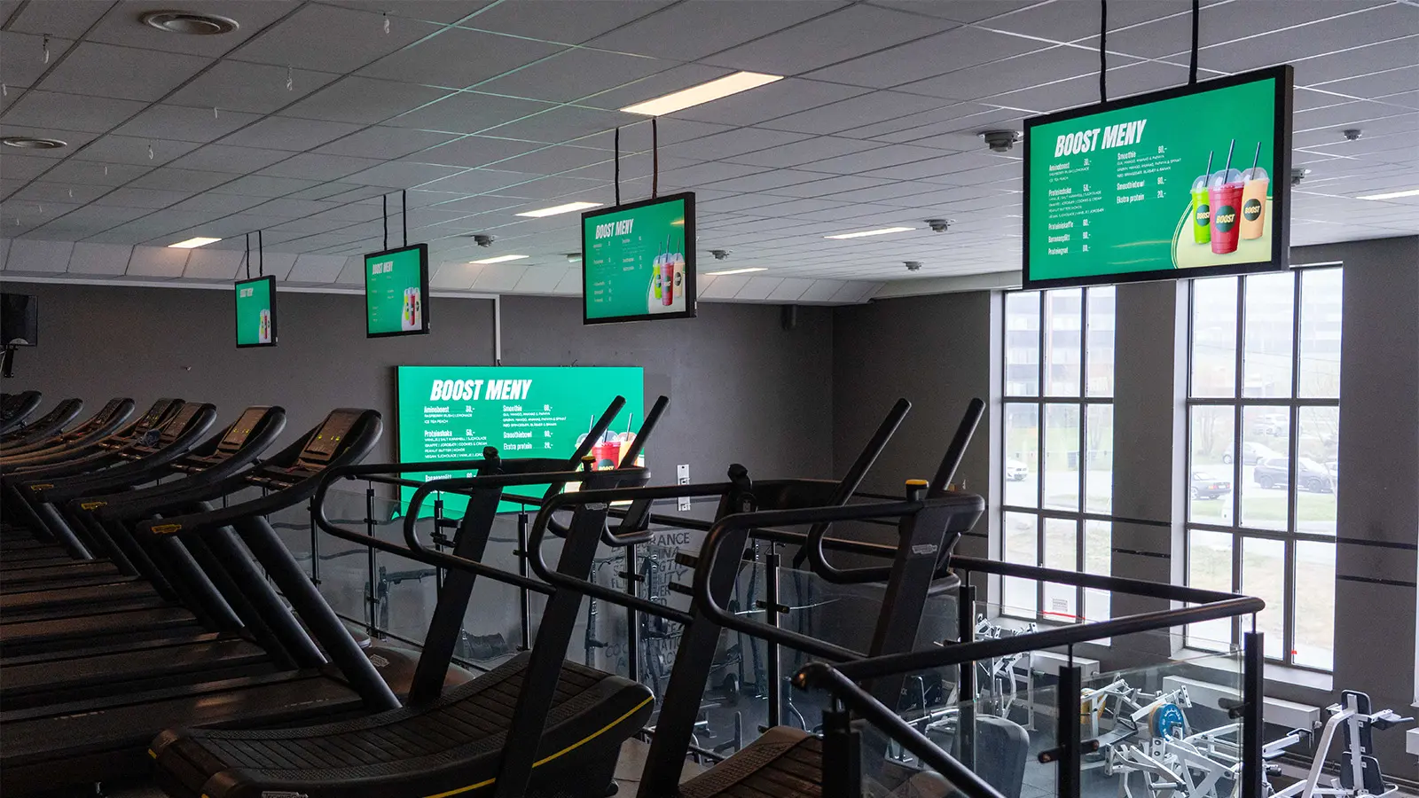 Cardio area with treadmills and digital signage screens displaying information throughout the gym.