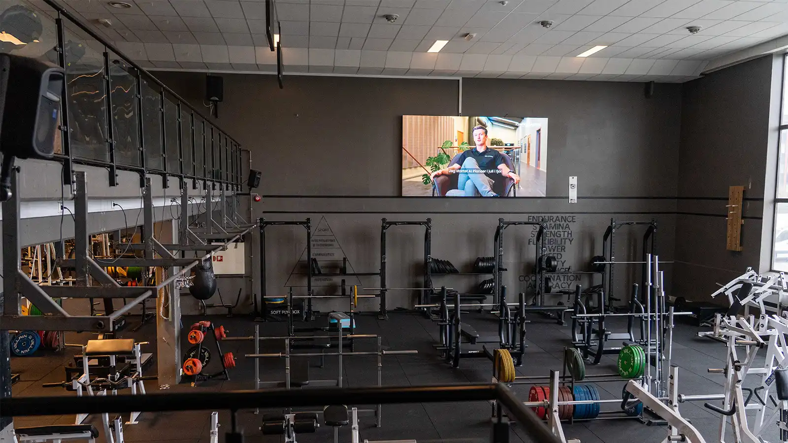 Strength training area with a large digital display mounted prominently on the wall.
