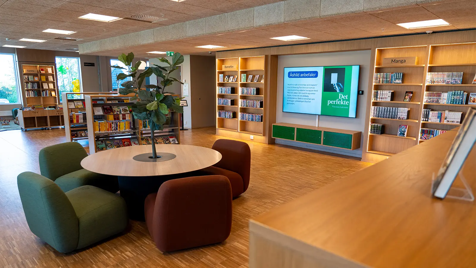 A digital information screen between bookshelves displaying a short book recommendation from a member of staff.
