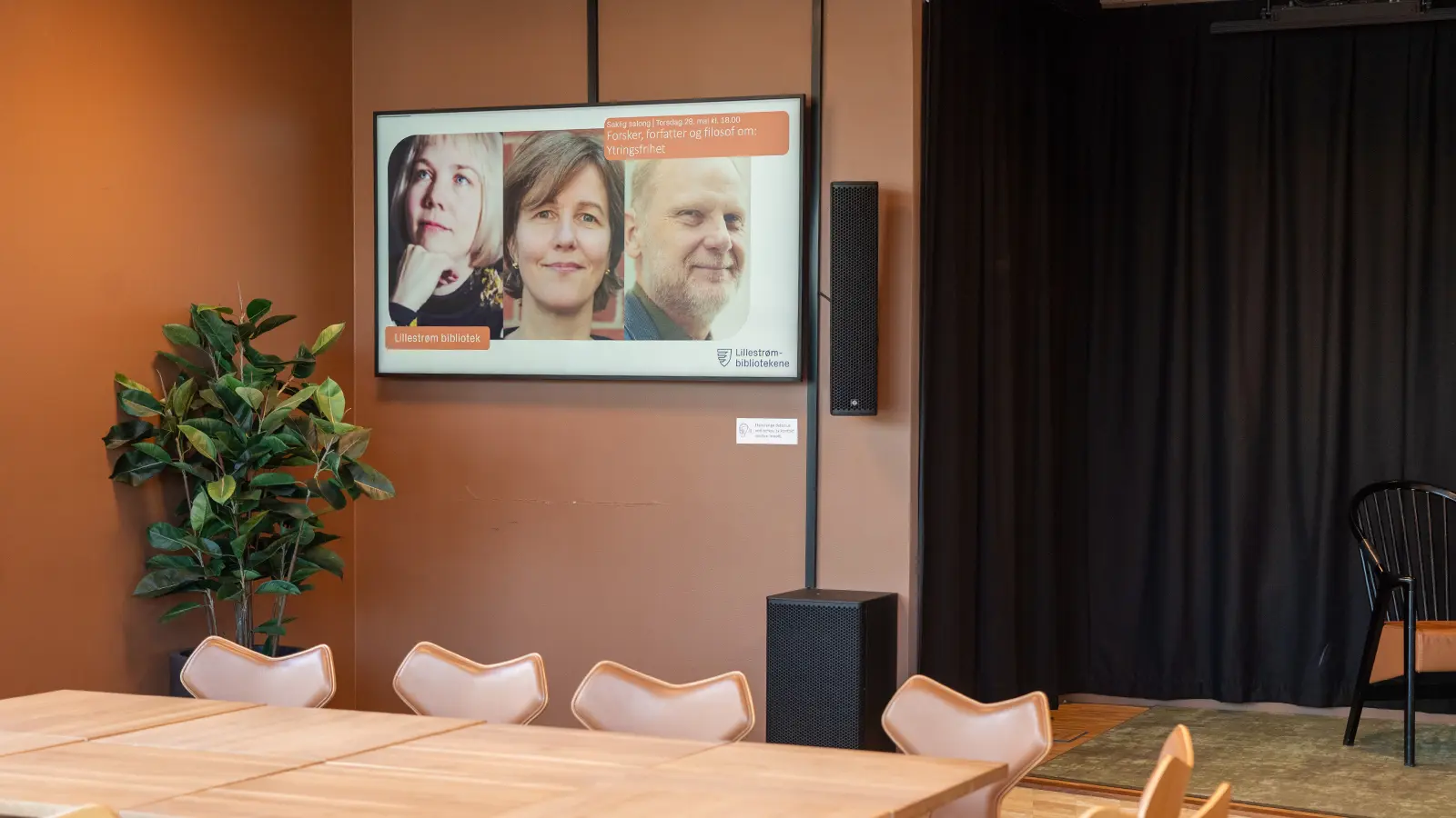 A digital information screen on the wall beside a group table in one of the library's work areas.