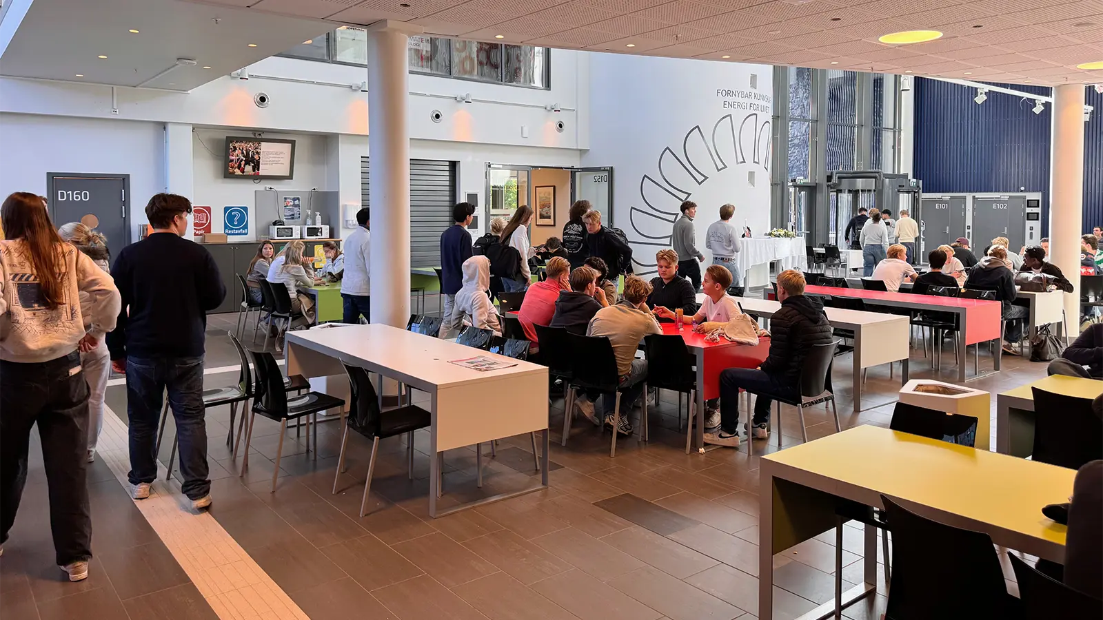 Students taking a break in the school cafeteria, with a digital signage screen mounted on the wall above them.