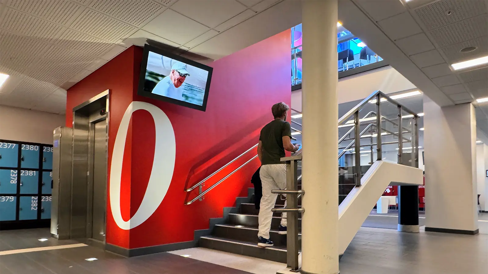A digital signage screen mounted on the wall in a busy school stairwell.
